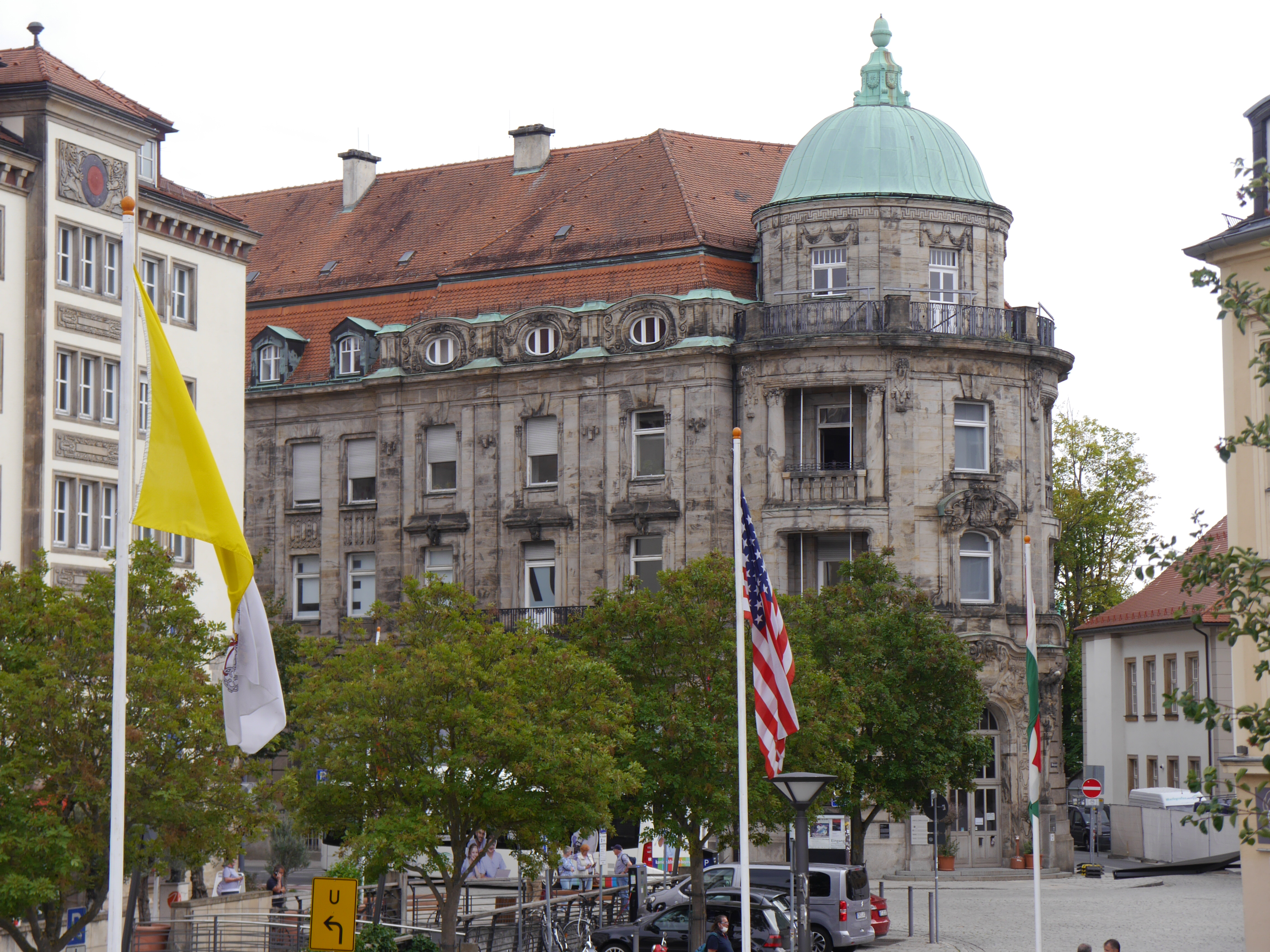 Farbfoto im Querformat. Blick von der Kanalstraße auf das Iwalewahaus. Es ist Sommer, die Bäume sind grün, es wehen die Fahnen wegen der Festspiele. Die dunkelgraue neobarocke Fassade des Iwalewahauses wirkt sehr repräsentativ.rungen nimm