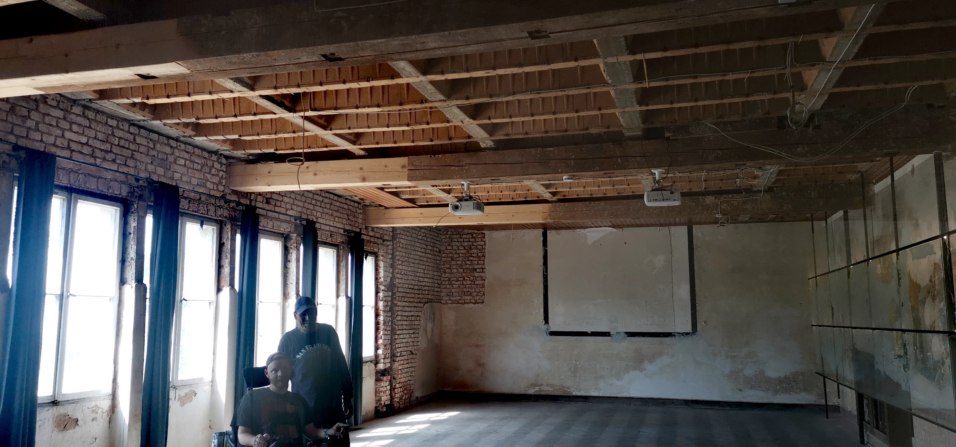 Farbfoto im Querformat. Blick in die Ausstellungshalle in Flossenbürg. Links eine durchfensterte Wand rechts das Kunstwerk von Talya Lubinski. Davor Benjamin Zorn und Philipp Schramm, die mit erhobenen Daumen den Erfolg ihrer Mission bekunden.